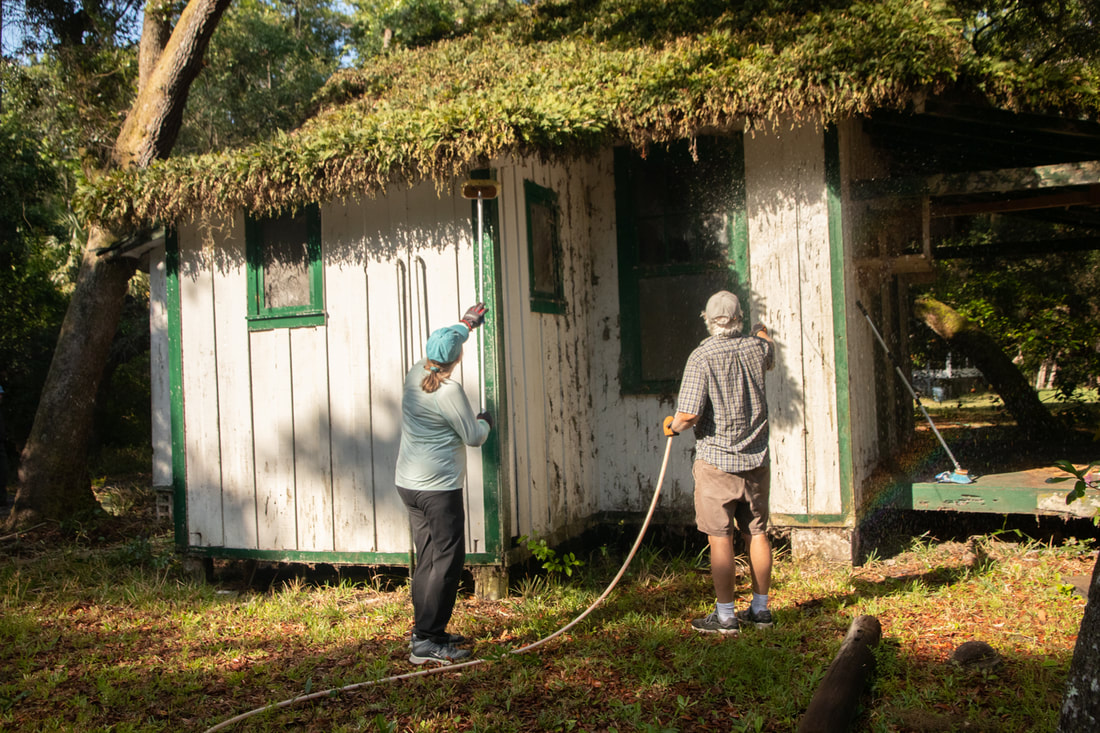 Picture of a male and female volunteer Working to sweep away the abundant spider webs and dirt
