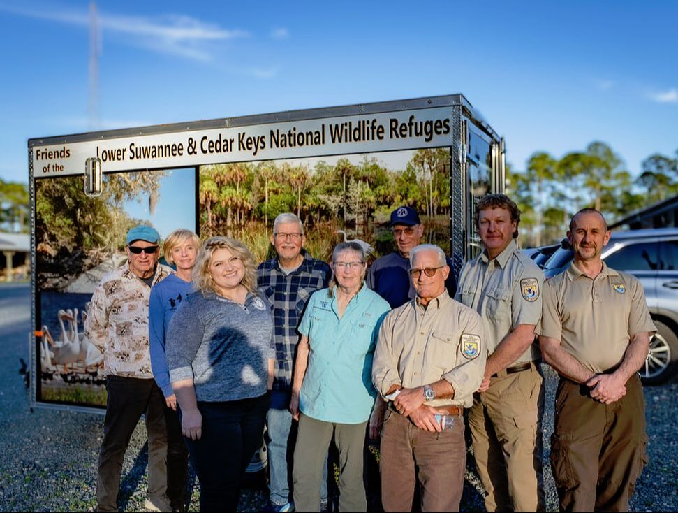 Picture of several Friends members and refuge staff members standing before the Friends' mobile outreach trailer