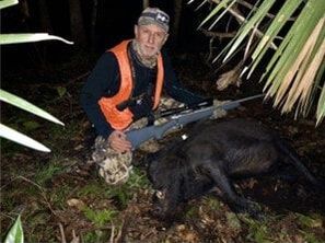 Picture of a hunter with rifle kneeling over a downed hog on the refuge